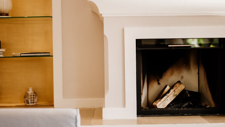 villa_schonthal-48_1, © Julius Hirtzberger Innenansicht eines Kamins mit Holzscheiten, daneben ein Regal mit Büchern und Dekoration.