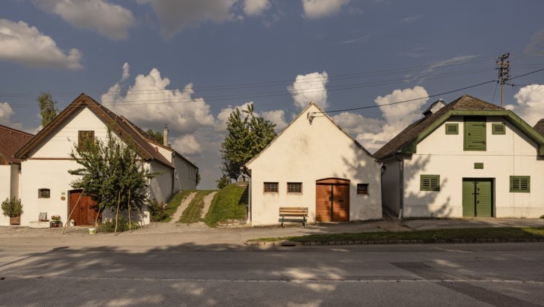 Kellergasse in Kettlasbrunn, © Weinviertel Tourismus / Schwarz-König Drei traditionelle Kellerhäuser in Kettlasbrunn unter blauem Himmel mit Wolken.