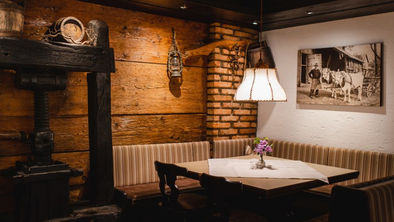 Platz nehmen in der gemütliche Gaststube, © Niederösterreich Werbung/Daniela Führer Gemütliche Gaststube mit Holzwänden, einer Eckbank, einem Tisch mit Blumen und einer Lampe. An der Wand hängt ein historisches Foto.