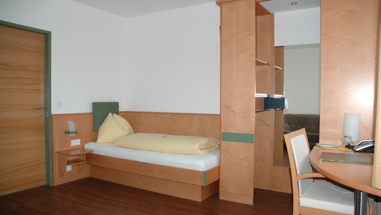 Hotel Zur Alten Schule, © Viregro Capital Gmbh Ein einfach eingerichtetes Hotelzimmer mit Einzelbett, Schreibtisch und Holzverkleidung.