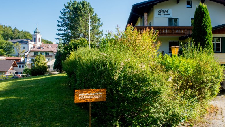 Pension, © Dorfschmiede eG Ein Gebäude mit der Aufschrift 'Dorfpension' und einem Schild 'Frühstückspension Mariahilfberg' in einer grünen Umgebung.