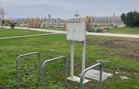 TDR-E- Bike Ladestation, © Donau NÖ, Fankhauser E-Bike Ladestation auf einer Wiese mit Fahrradständern und einem Weg im Hintergrund.