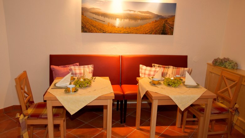 Frühstücksraum, © www.wachaufoto.at Gemütlicher Frühstücksraum mit zwei gedeckten Tischen, roten Sitzbänken und einem Landschaftsbild an der Wand.