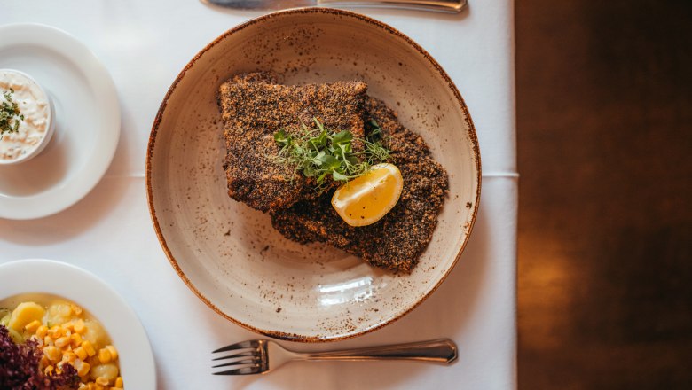 Waldviertler Karpfenfilet vom Stift Zwettl in Graumohn paniert, © Niederösterreich Werbung/Daniela Führer Graumohn-paniertes Karpfenfilet mit Zitronenscheibe und Kräutern auf Teller, daneben Beilagen.