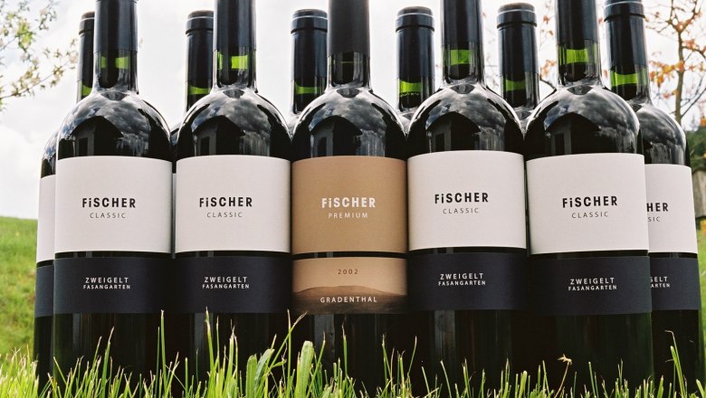 Weine, © Weingut Fischer Mehrere Weinflaschen der Marke Fischer stehen im Gras.