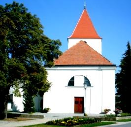 KircheHaringsee, © Gemeide Haringsee Weiße Kirche mit rotem Dach und Turm, umgeben von Bäumen.