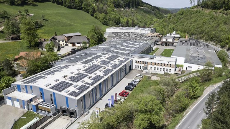 Schmid Schrauben Hainfeld GmbH, © Schmid Schrauben Hainfeld GmbH Luftaufnahme einer großen Fabrikanlage mit Solarpanelen auf den Dächern, umgeben von grüner Landschaft.