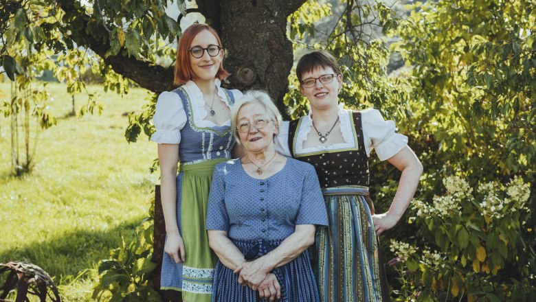 Generationsübergreifende Frauenpower, © Niederösterreich Werbung/David Schreiber Drei Frauen in traditioneller Tracht stehen lächelnd unter einem Baum im Freien.
