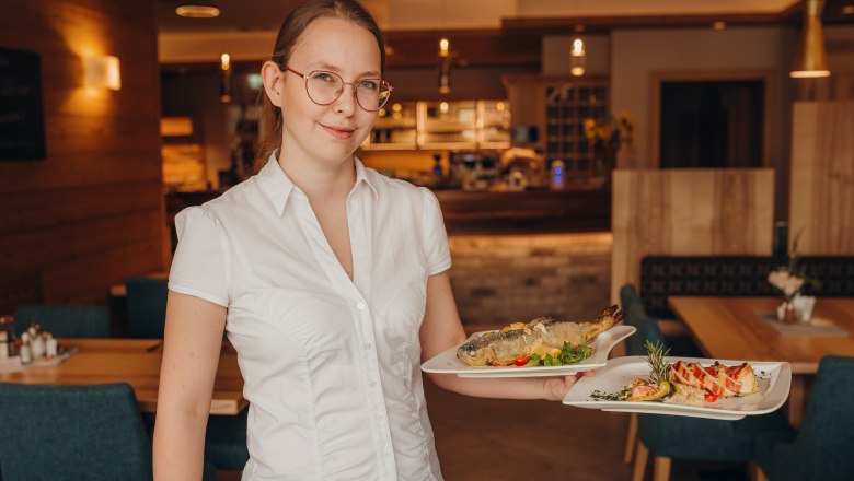Tochter Victoria Froschauer, © Niederösterreich Werbung/Daniela Führer Eine Frau in einem Restaurant trägt zwei Teller mit Speisen.