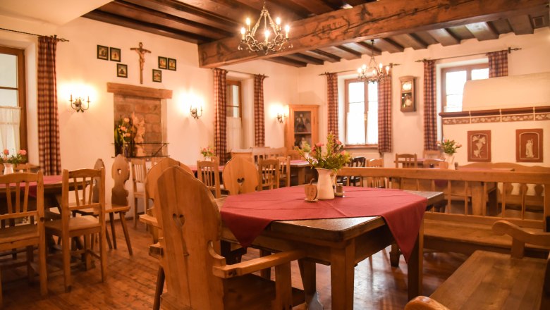 Stube, © Genussbauernhof Böhm Gemütliche Stube mit Holzmöbeln, roten Tischdecken und Kronleuchtern.