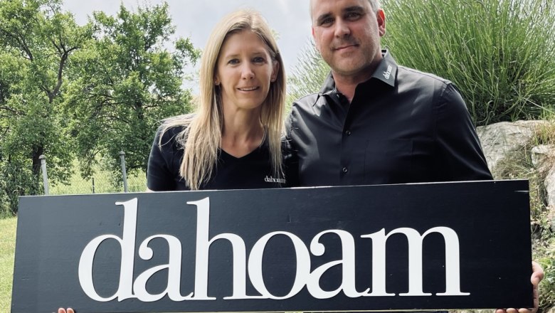 Die Gastgeber im "dahoam", © Anita Gradwohl, dahoam Zwei Personen halten ein Schild mit der Aufschrift 'dahoam' im Freien.