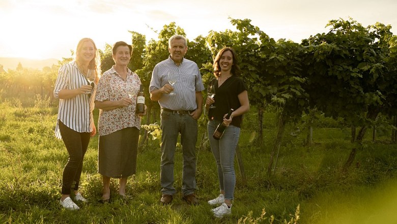 walzer-johann-62, © Weinbau Johann Walzer Vier Personen stehen in einem Weinberg und halten Weingläser und Flaschen in der Hand.