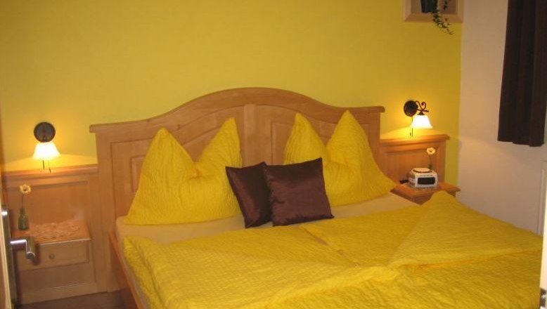 Gästezimmer, © Fam. Schwalm Gemütliches Gästezimmer mit gelber Bettwäsche und Holzmöbeln.