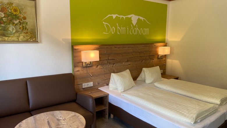 Doppelzimmer, © Wiener Alpen Gemütliches Doppelzimmer mit Holzmöbeln, Sofa, Tisch und Wanddekoration.