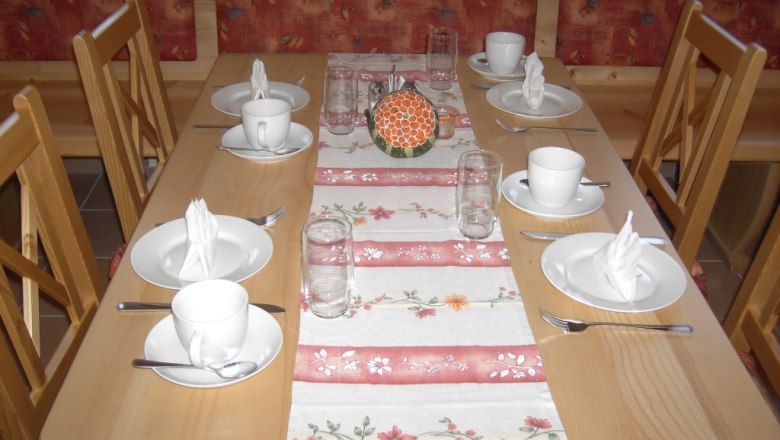 Frühstücksraum, © Gästehaus Denk Ein gedeckter Tisch in einem Frühstücksraum mit Geschirr und Gläsern.