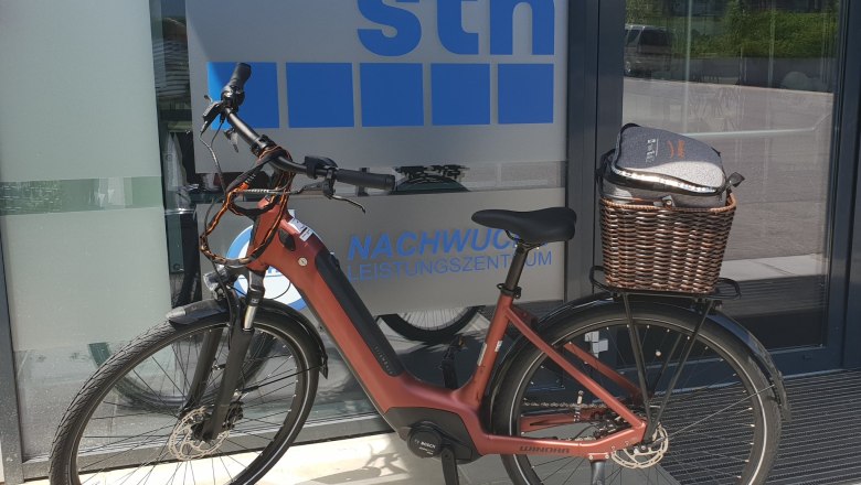 eBike Verleih, © Stadthotel Hollabrunn Ein rotes E-Bike steht vor einem Gebäude mit der Aufschrift 'sth Nachwuchsleistungszentrum'.
