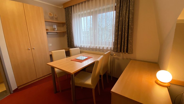 Ferienwohnung Herbst, © Privatzimmer Leeb Ein gemütlicher Raum mit Holzmöbeln, Tisch, Stühlen und einem Fenster mit Vorhängen.