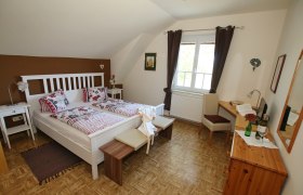 Gästezimmer, © Wolfgang Hanousek Gemütliches Gästezimmer mit Doppelbett, Sofa, Tisch und Stuhl. Braune Akzentwand und dunkle Vorhänge.