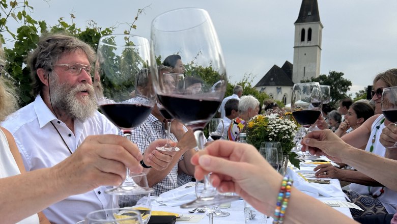 Tafeln im Weinviertel, © Weinviertel Tourismus GmbH Menschen stoßen mit Weingläsern an einem langen Tisch im Freien an, im Hintergrund eine Kirche.