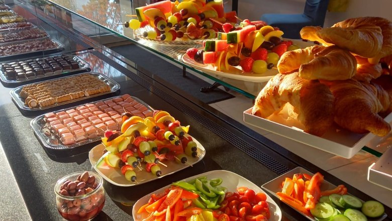 Sonntagsbrunch, © Kaffeeliebe Ein Buffet mit Croissants, Obstspießen, Gemüse und Oliven in einem sonnendurchfluteten Raum.