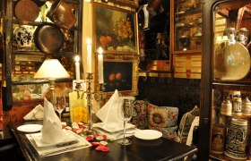 Marchfelderhof, © Gault Millau Gemütlich dekorierter Tisch in einem rustikalen Restaurant mit Kerzenleuchter, Bildern und antiken Gegenständen.