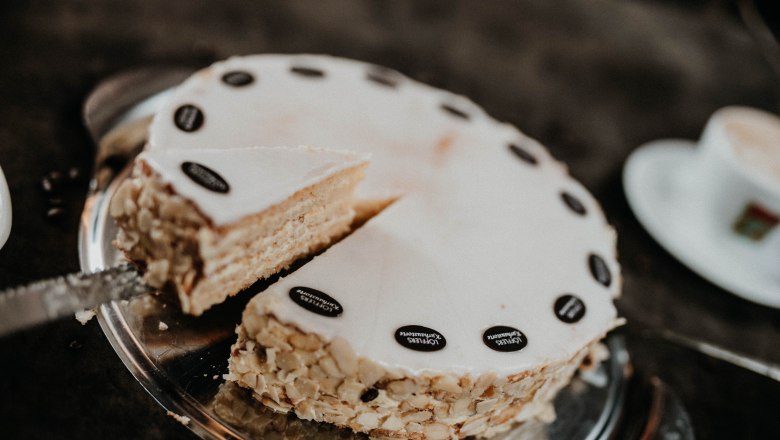 Hausgemachte Torten, © Nicole Seiser Eine angeschnittene Torte mit Mandeln und Schokoladendekoration auf einem Tablett.