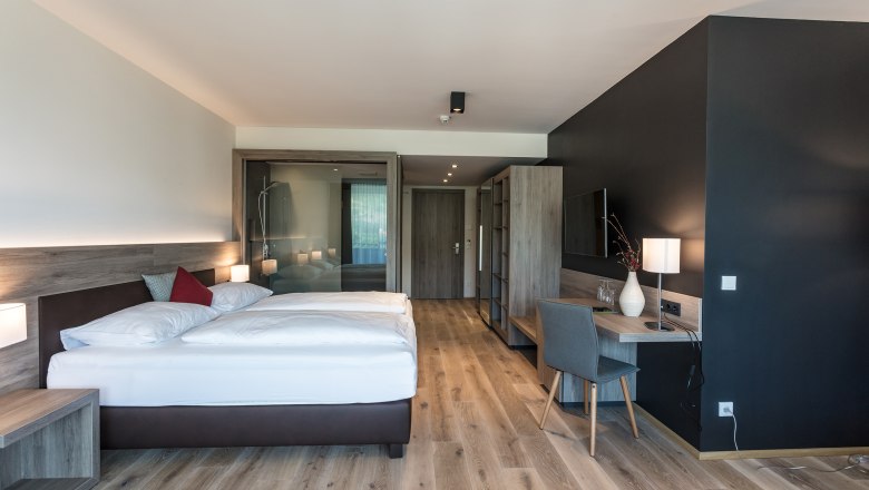 Großzügiges Zimmer in der Weinlodge, © KASTNER NEW MEDIA - kastner.tv Modernes Hotelzimmer mit Doppelbett, Schreibtisch und Holzfußboden.