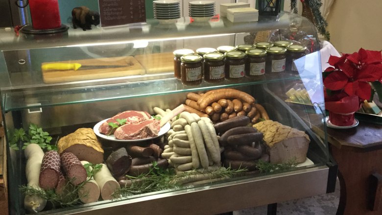 Hofladen, © Kogelhof Eine Fleischtheke in einem Hofladen mit verschiedenen Wurstsorten, Fleischstücken und Gläsern mit Aufstrichen.