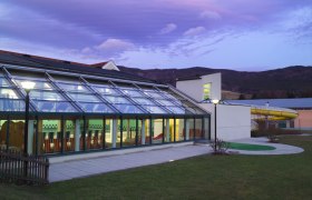 Hallenbad Yspertal, © Hallenbad Yspertal Außenansicht des Hallenbads Yspertal bei Dämmerung mit Glasfassade und Rutsche.