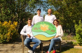 Familie Bachl, © Jakob Bachl Vier Personen posieren mit einem Schild von 'Bachl's Feldgemüse' in einem Garten.