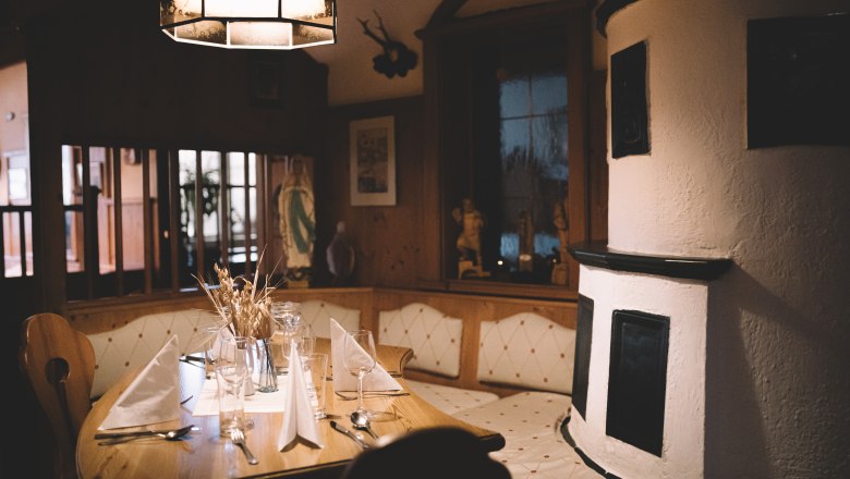 Heimelige Stube & Terrasse mit Wallfahrtskirchen-Blick, © Niederösterreich Werbung/Mara Hohla Gemütliche Stube mit Holztisch, gedeckt mit Gläsern und Servietten, daneben ein traditioneller Kachelofen.
