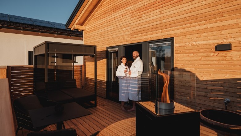 Terrasse mit Himmelbett und Feuerstelle, © Chalaalets Terrasse mit Himmelbett, Feuerstelle und zwei Personen in Bademänteln.