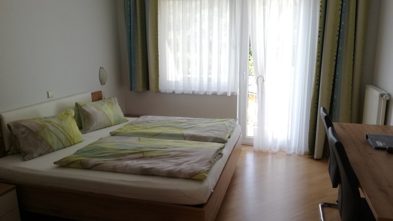 Doppelzimmer Mit Balkon, © Familie Langthaler Ein Doppelzimmer mit einem Bett, einem Tisch und einem Balkon mit Vorhängen.