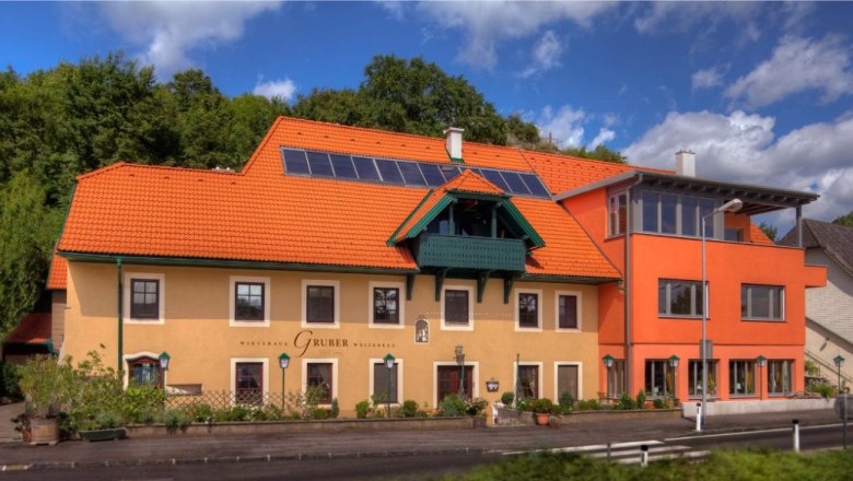 Wirtshaus, © wirtshausgruber.at Ein traditionelles Wirtshaus mit orangefarbenem Dach und Solarpanelen, umgeben von grüner Natur.