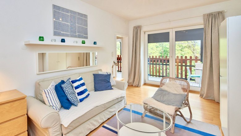 Top 2 - Wohnzimmer, © VP FeWo OG Modernes Wohnzimmer mit Sofa, Kissen, Glastisch und Balkon.