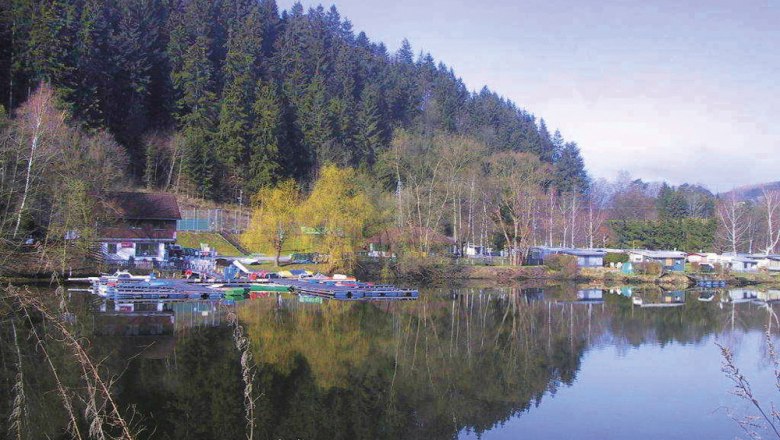 Seecamping in Krumau am Kamp, © Seecamping & Freizeitanlage Krumau/Kamp Seecampingplatz mit Wohnwagen und Booten am Ufer eines Sees, umgeben von Wald.