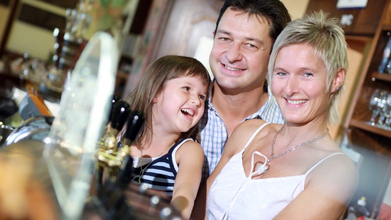 Hotel zur Post, © weinfranz.at Eine lächelnde Familie steht in einem Restaurant oder Hotel an der Bar.