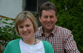 Winzerpaar, © Fam. Zuckriegl Ein lächelndes Paar steht im Freien vor einer grünen Hecke.