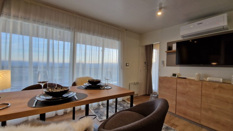 Wohnzimmer Johannesbachklamm Chalet, © Johannesbachklamm Chalet Modernes Wohnzimmer mit Esstisch, Stühlen, großem Fenster und Fernseher.