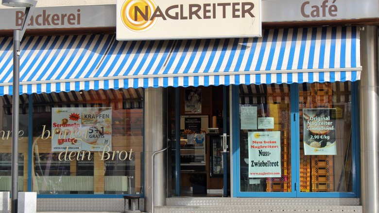 Bäckerei&Konditorei Naglreiter Fischamend, © Donau Niederösterreich Birgit Köck Eingang einer Bäckerei mit blau-weiß gestreifter Markise und Schildern für Angebote.