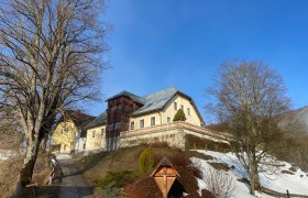 Garhof im Winter, © Wiener Alpen Ein großes Gebäude auf einem Hügel mit Schnee und kahlen Bäumen im Vordergrund.