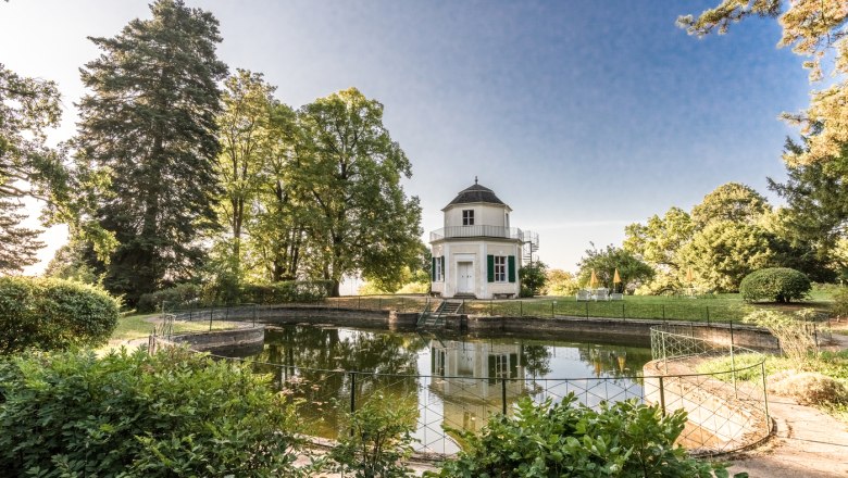 badepavillon, © Schloss Artstetten Ein achteckiger Pavillon steht neben einem Teich, umgeben von Bäumen und Garten.