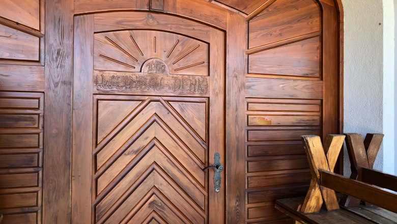 Heurigenlokal Denk, © Donau Niederösterreich Holztür mit der Aufschrift 'Weinbau Denk' und einer Sonne darüber.