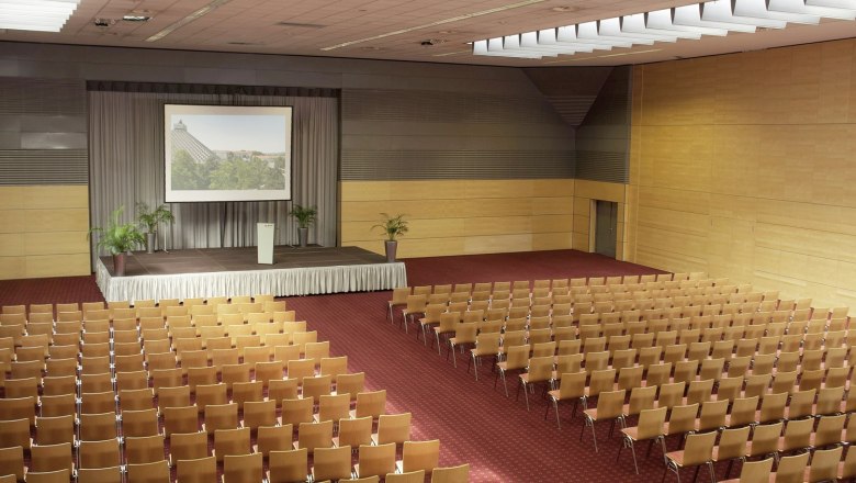 Eventhotel Pyramide, Europa Saal 4, © Eventhotel Pyramide GmbH Großer Konferenzsaal mit Bühne und Stuhlreihen.