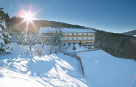 Gasthof-Pension Ödenhof, © Ödenhof, Foto: Franz Zwickl Ein verschneites Gebäude mit der Aufschrift 'Ödenhof' in einer winterlichen Landschaft, umgeben von Bäumen und strahlendem Sonnenschein.