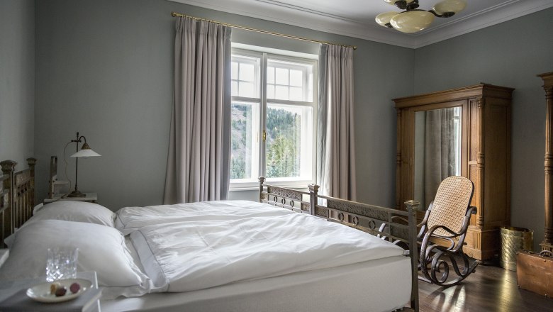 Villa Antoinette, © Matthias Kronfuss Elegantes Schlafzimmer mit antikem Bett, Schaukelstuhl und großem Fenster mit Vorhängen.