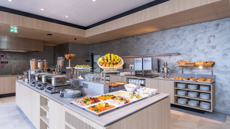 Frühstücksbuffet, © Hilton Garden Inn Wiener Neustadt Ein reichhaltiges Frühstücksbuffet mit Obst, Gebäck, Aufschnitt und Cerealien in einem modernen Hotelrestaurant.