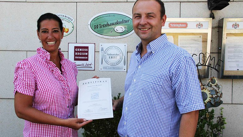 smostlandl, © Leopold Rank Zwei Personen halten ein Zertifikat vor einer Wand mit Auszeichnungen.