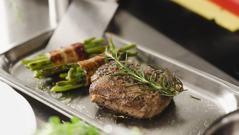 Regionale Fleischqualität & Spezialitätenküche von Spargel bis Kürbis, © Niederösterreich Werbung/Michael Reidinger Ein Steak mit Rosmarin und Bohnen im Speckmantel auf einem Metalltablett.