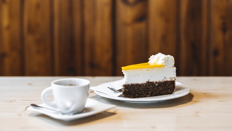 Eierlikörtorte, © Niederösterreich Werbung/David Schreiber Stück Kuchen mit Sahne und Tasse Kaffee auf Holztisch.